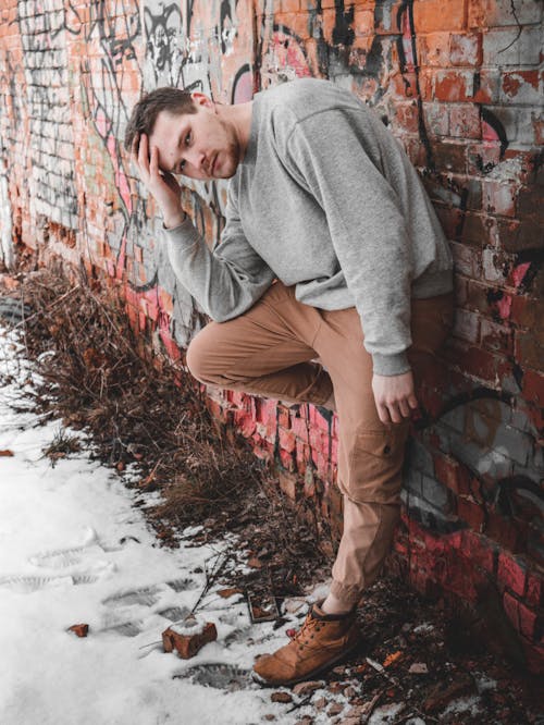 Young Man Posing in Front of a Brick Wall Covered in Graffiti