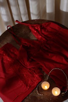 Intimate setting with red lace lingerie and tealight candles on a wooden table.