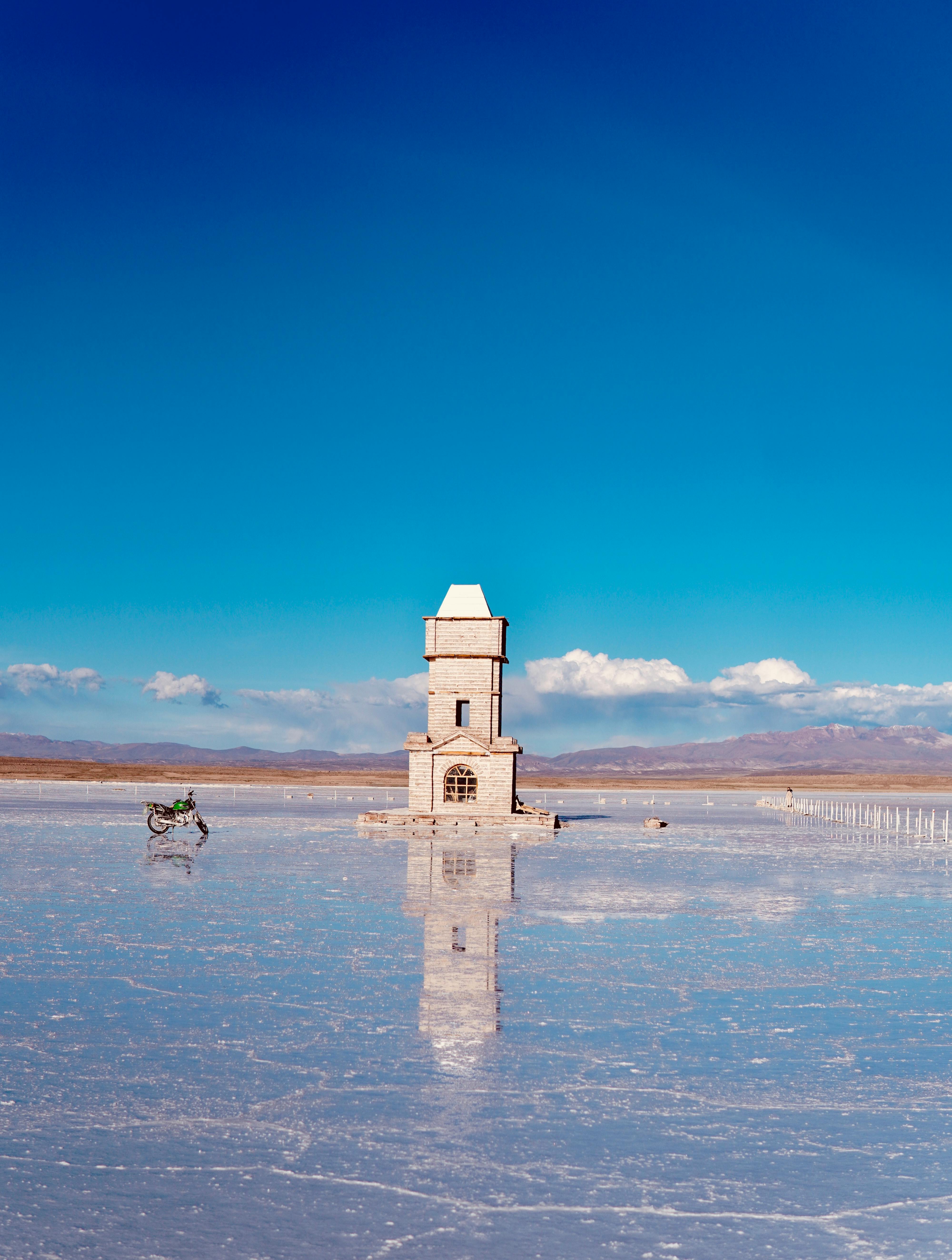 An isolated tower reflected on a frozen lake under a clear sky, symbolizing solitude.