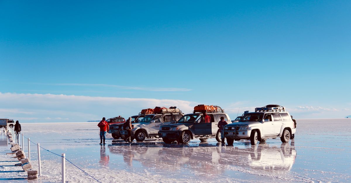 4x4 cars parked on a reflective salt flat under a clear blue sky, ideal for adventure stock photos.