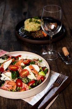 Delicious smoked salmon salad with cherry tomatoes and cheese, paired with an empty wine glass.