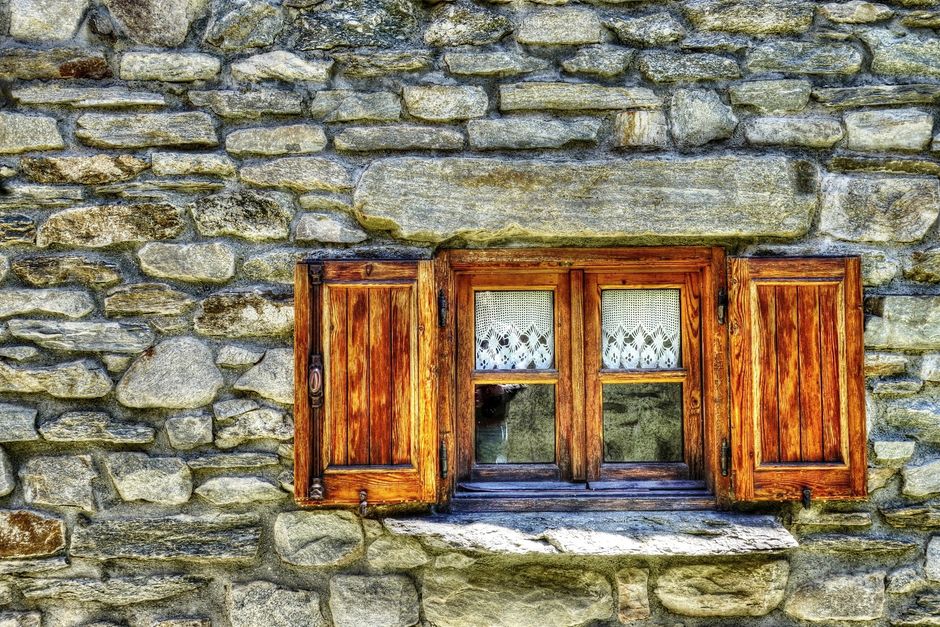 Close-up of a vintage stone wall featuring a classic wooden window, emphasizing rustic charm.
