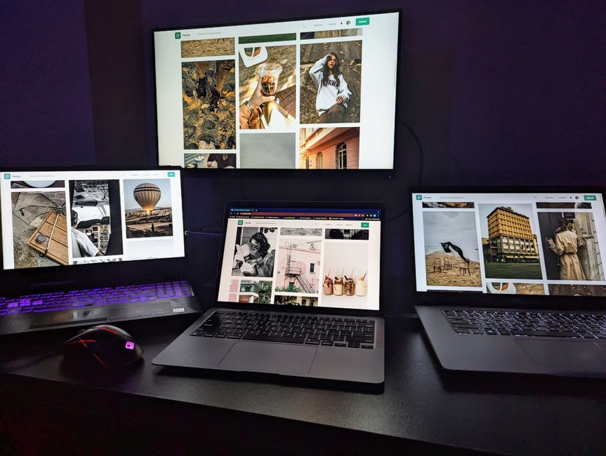 Three laptops and a monitor on a desk displaying creative graphic designs. Perfect for tech-focused projects.