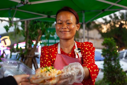 A cheerful woman in Phnom Penh serving tasty street food with a warm smile.
