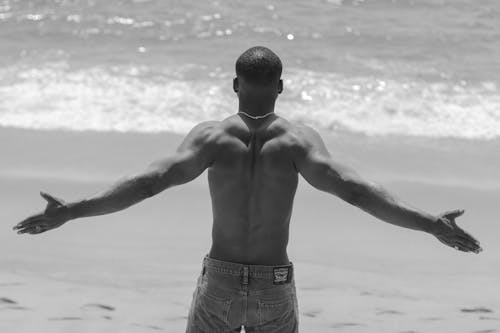 Back View of a Shirtless Man Standing on the Beach with His Arms Spread 