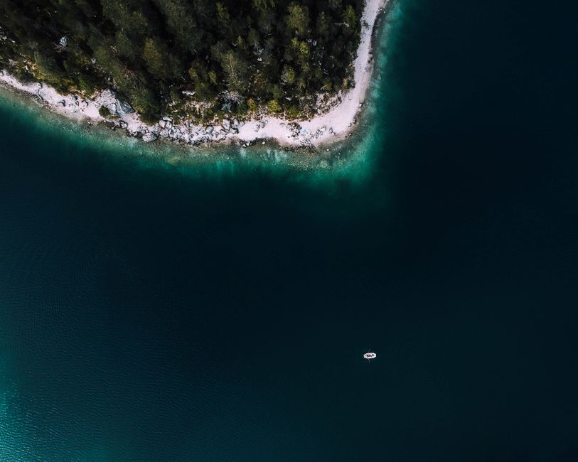 A serene aerial shot of a boat on a clear turquoise lake beside a forested shoreline.