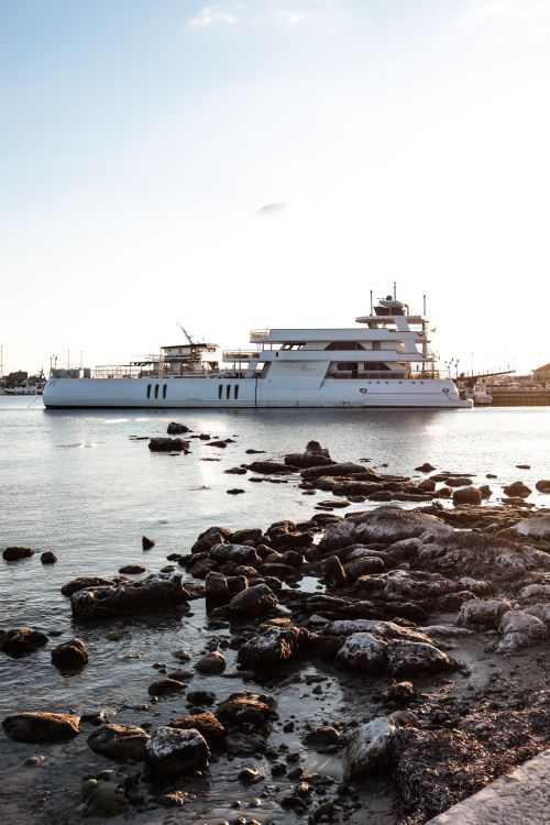 Free Stunning view of a luxury yacht moored near rocky shore at sunset, capturing serene maritime beauty. Stock Photo