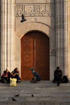 A group of people sitting on steps outside a historic Ottoman style door in Istanbul, Türkiye.