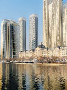 Stunning cityscape of modern skyscrapers by a tranquil waterfront, under a bright blue sky.