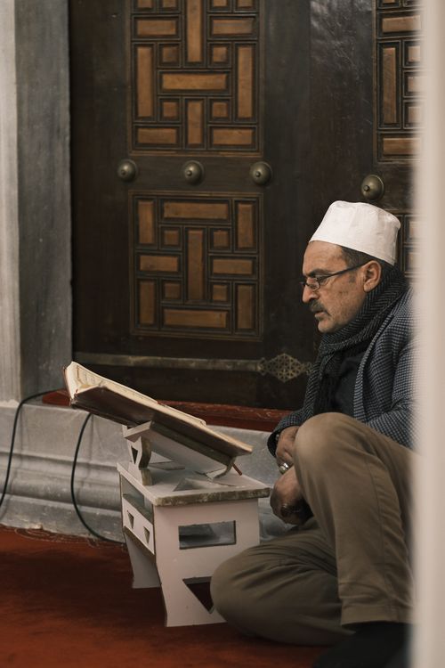 Free A man sits on the floor of a mosque, reading a book, conveying a serene and introspective moment. Stock Photo
