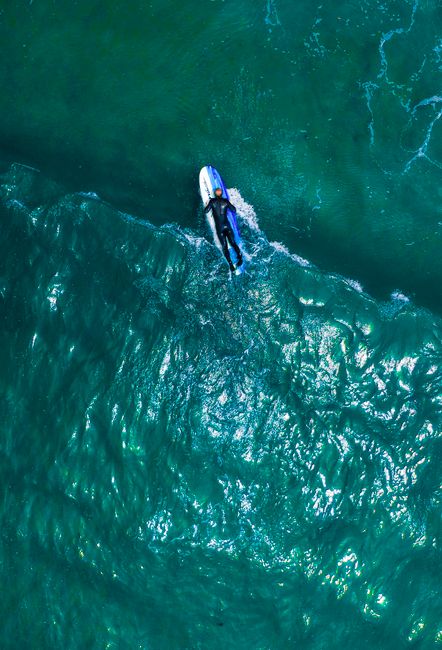 Dynamic aerial shot of a surfer on a wave showcasing the vibrant blue ocean from above.