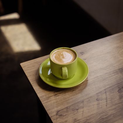 Cappuccino in a green cup on a wooden cafe table, photo by Rivero on Pexels