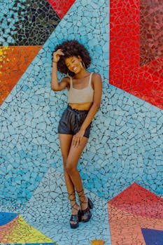 Cheerful woman in casual fashion posing by vibrant mosaic wall outdoors.
