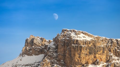 Free A stunning view of a snow-capped mountain peak against a bright blue sky with the moon visible in the background. Stock Photo