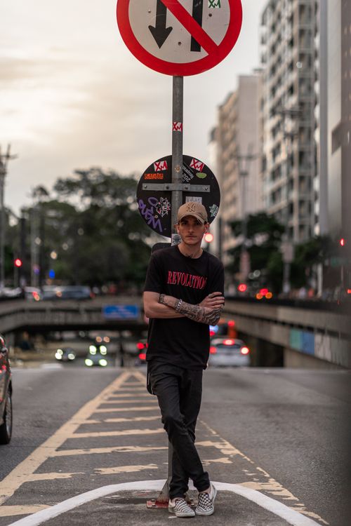 Free A stylish man with tattoos poses on a city street beneath a road sign. Stock Photo