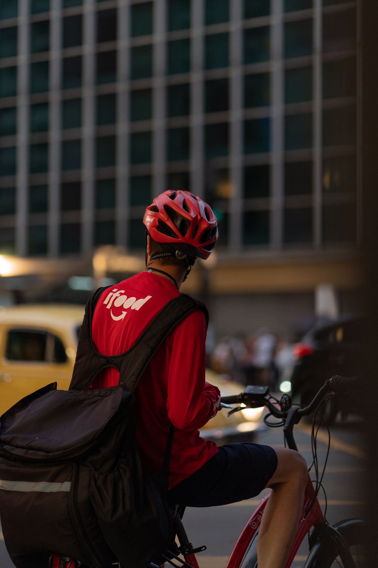 Helmeted bicycle courier carrying a bag while riding through an urban setting