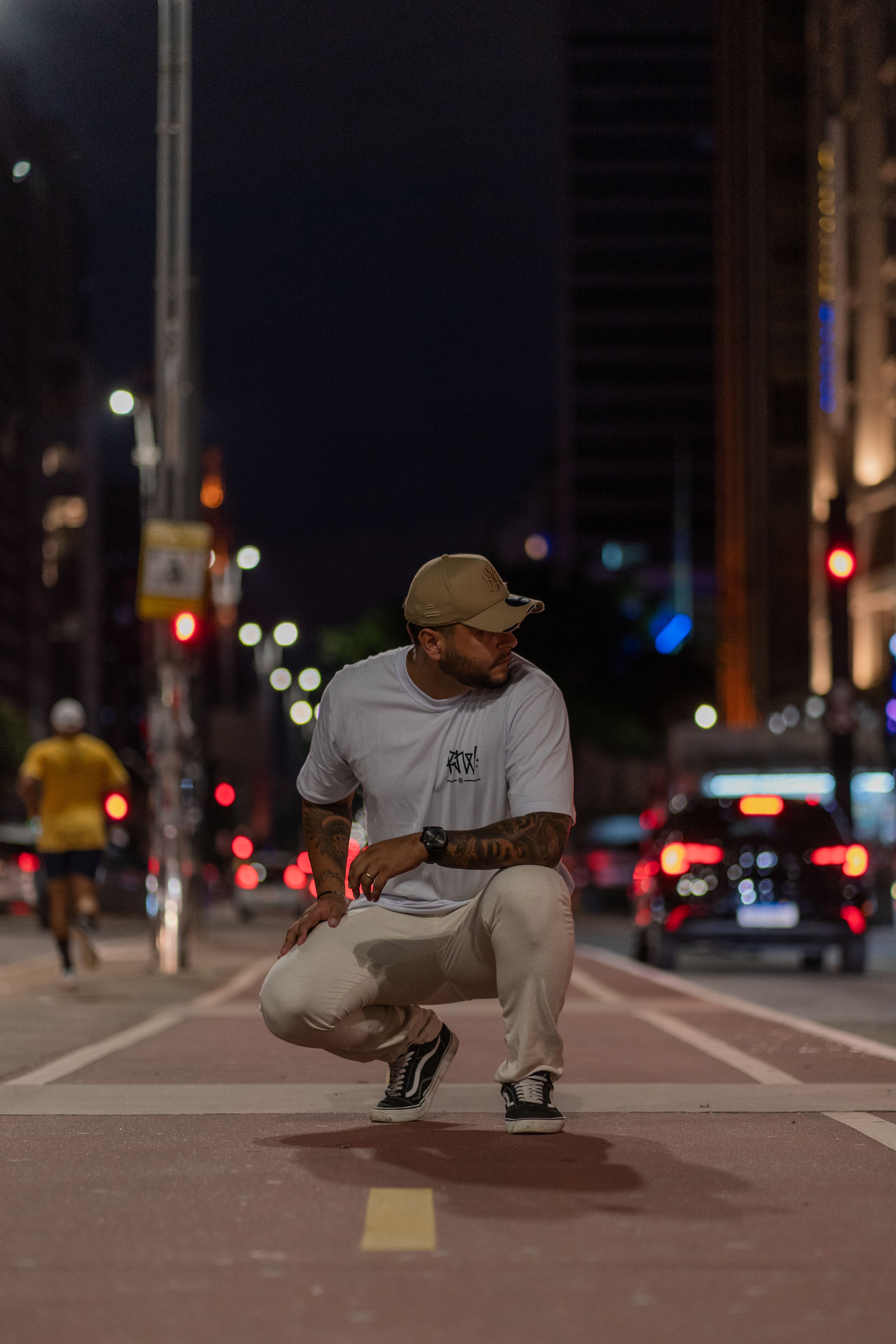 A man crouching in an urban street at night, surrounded by city lights and traffic.