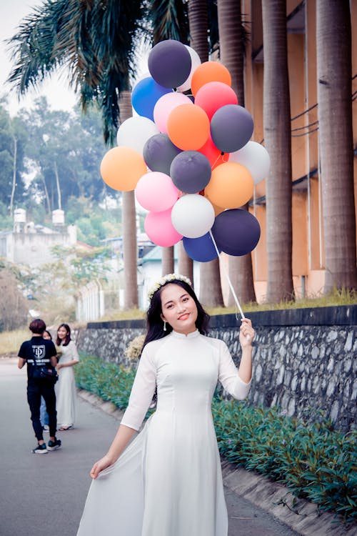 Free Woman Wearing White Dress While Holding Bundle of Balloons Stock Photo