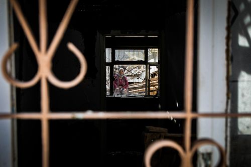 Free A woman stands behind a barred window in a dark, destroyed interior. Stock Photo