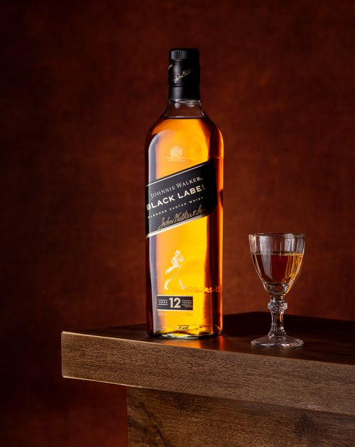 Free Elegant Johnnie Walker Black Label whisky bottle with a glass against a red backdrop. Stock Photo