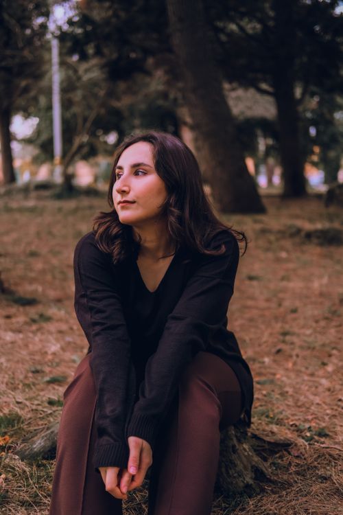 Free Woman in black sweater sitting in forest, surrounded by trees. Stock Photo