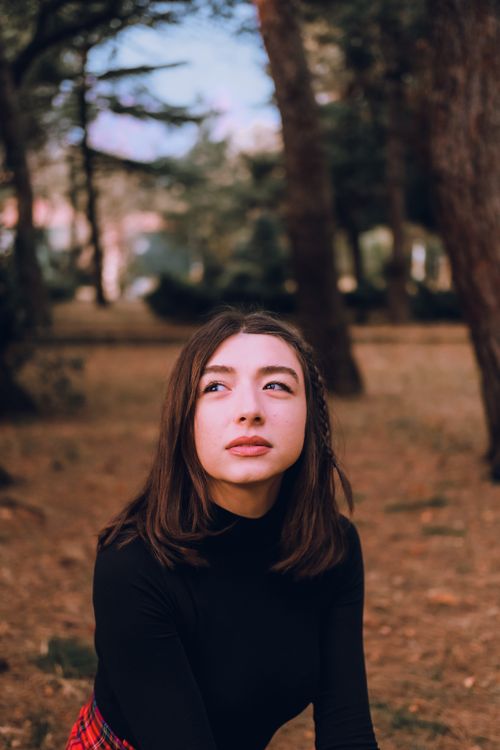Free A thoughtful woman in a black top poses amidst nature in a tranquil park. Perfect for lifestyle and fashion themes. Stock Photo