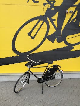 A black bicycle parked against a striking yellow mural depicting cyclists.