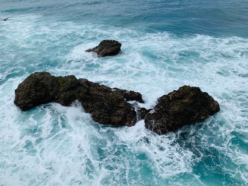 Free Captivating aerial shot of rugged rocks and waves on a vibrant coastline. Stock Photo
