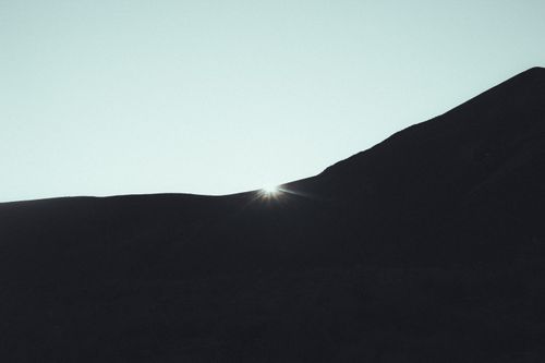 Free Capture of sunlight peeking over a hill silhouette under a clear sky at dawn, serene and tranquil. Stock Photo