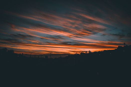 Capture the beauty of a vibrant sunset with colorful clouds and urban silhouette.