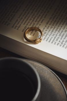 A close-up of a golden snake ring resting on an open book beside a coffee cup.