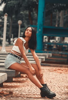 Young woman sitting on a bench outdoors with a confident pose, highlighting summer fashion.