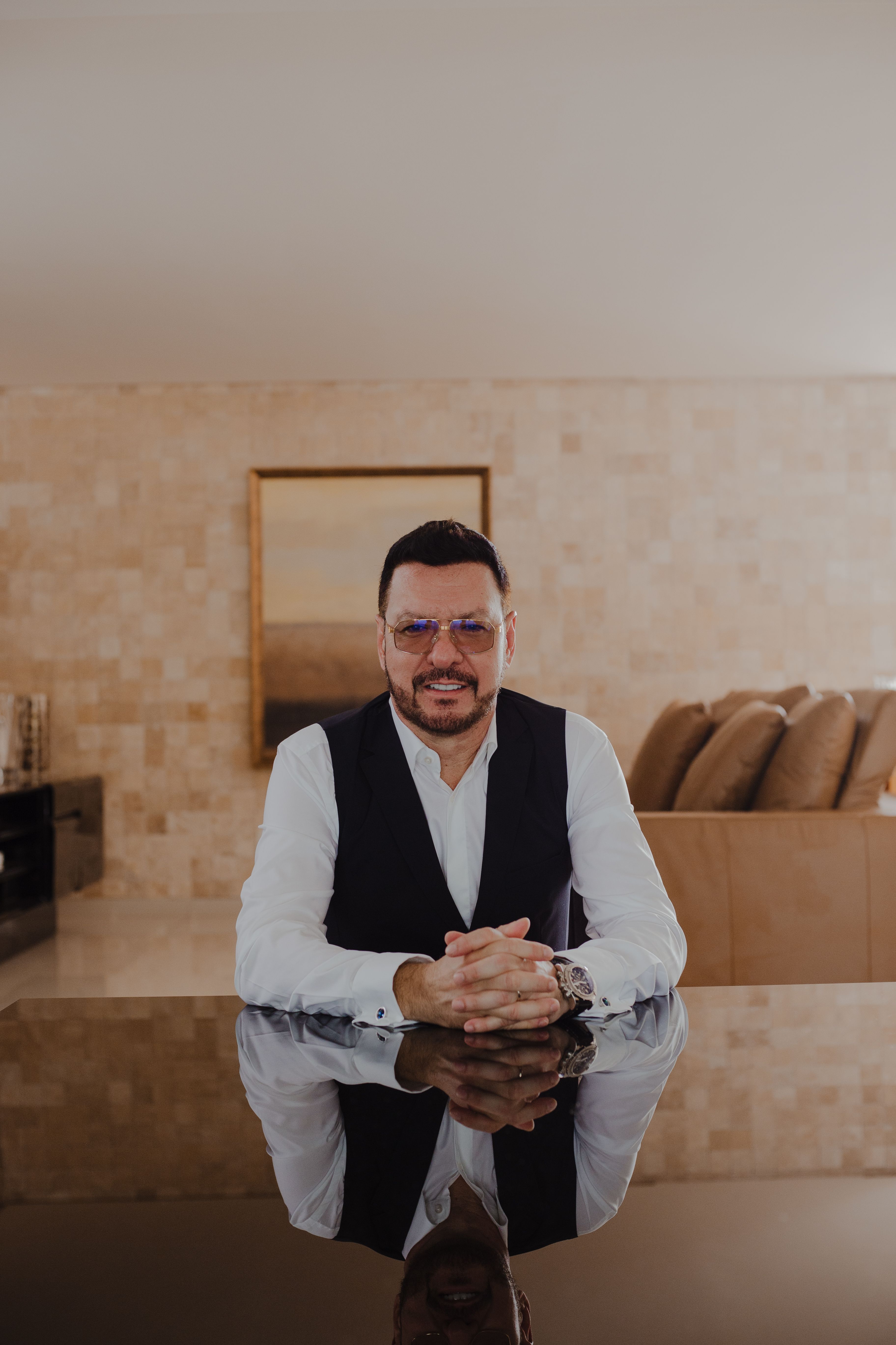 Elegant portrait of a man in a vest at home, reflecting on a glass table surface.