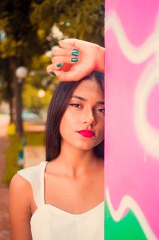 Fashionable woman posing against colorful wall outdoors, showcasing style and confidence.