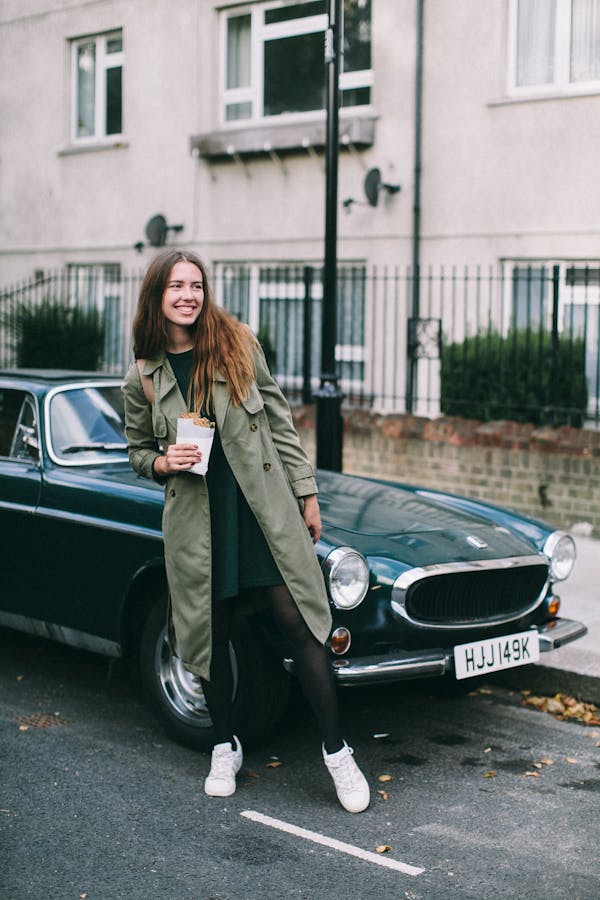 woman smiling in overcoat holding a cup of coffee standing in front of black car