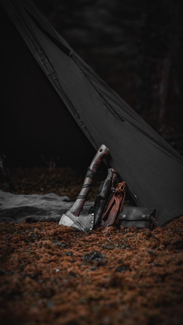 Axe and knives on mossy ground by a tent, perfect for a camping adventure