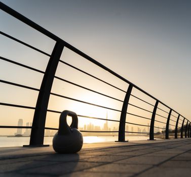 A kettlebell on a waterfront promenade in Dubai at sunset with the city skyline in the background.