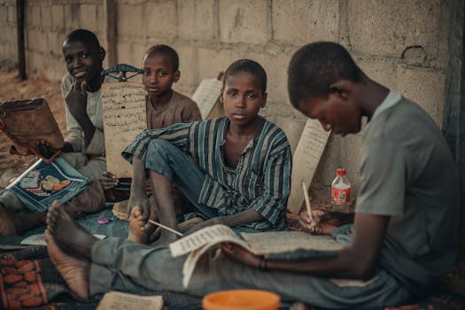 A group of African boys studying outdoors in Kano, Nigeria, with Arabic writings.