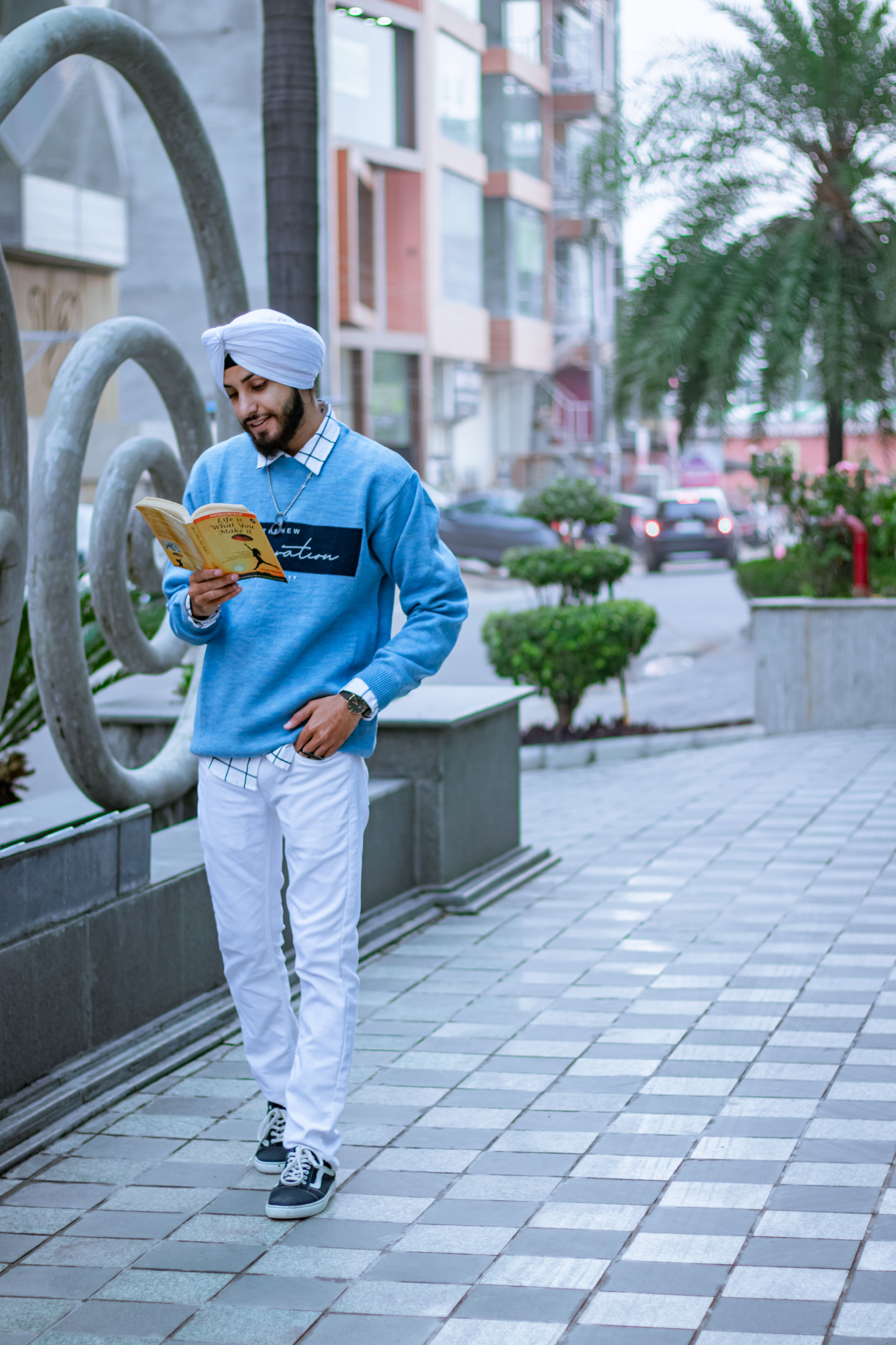 A man in a turban reads a book on a city street, exemplifying urban lifestyle.