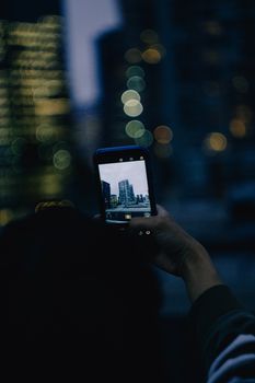 A person holds a smartphone capturing Seattle's skyline against a blurred urban backdrop at twilight.