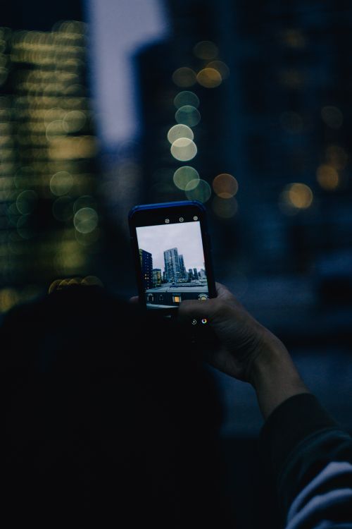 Free A person holds a smartphone capturing Seattle's skyline against a blurred urban backdrop at twilight. Stock Photo