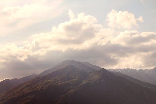 Breathtaking mountain scene with clouds drifting over rugged peaks under a backlit sky.