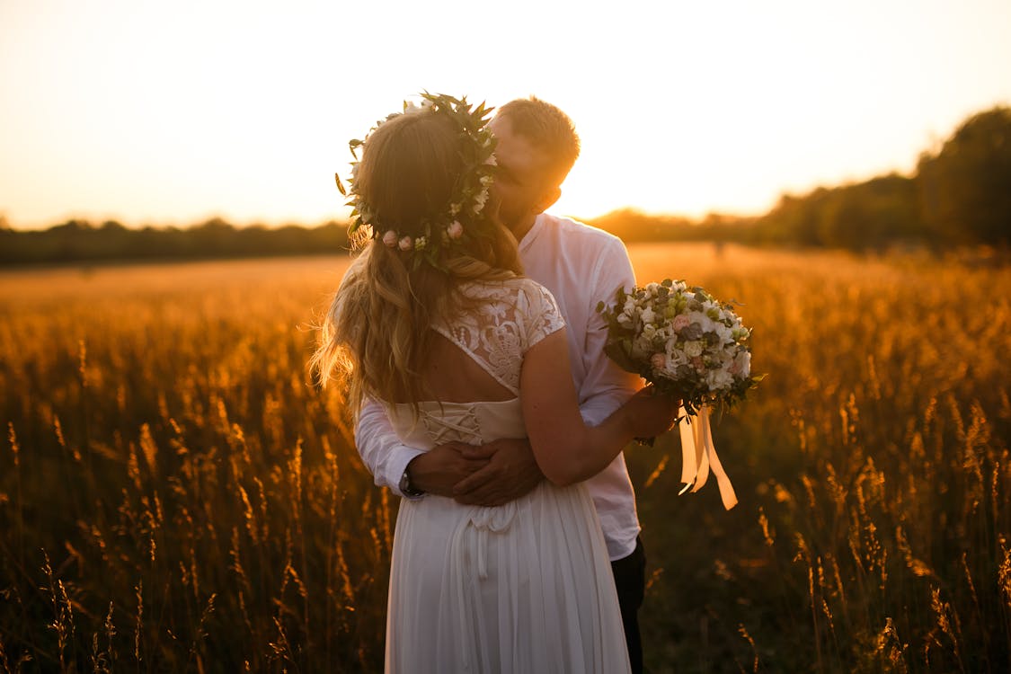 Free Man and Woman Standing in Front of Brown Grass Field Kissing Each Other Stock Photo