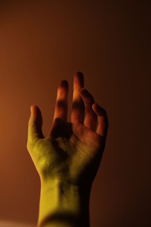 Free Close-up of a human hand in dramatic lighting with warm tones and shadows, creating a mysterious atmosphere. Stock Photo