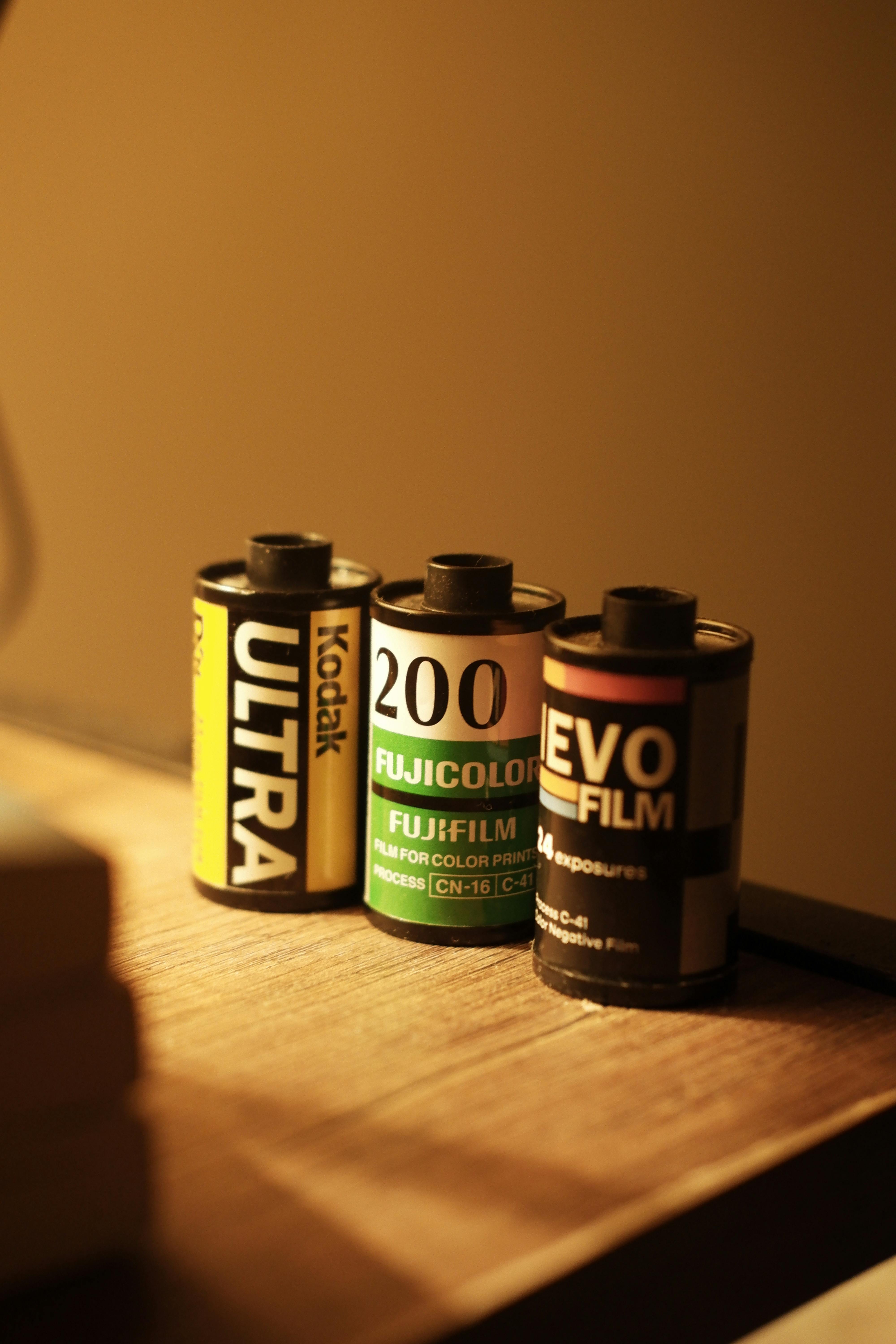 Three vintage film rolls from different brands on a wooden surface, warm lighting.