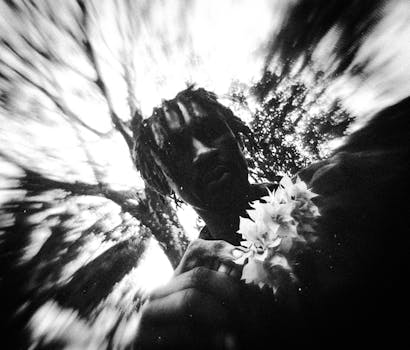 A moody black and white portrait of a person outdoors holding flowers, capturing a surreal atmosphere.