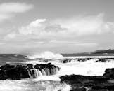 这是一张引人注目的黑白照片，在多云的天空下，海浪正撞击着岩石海岸