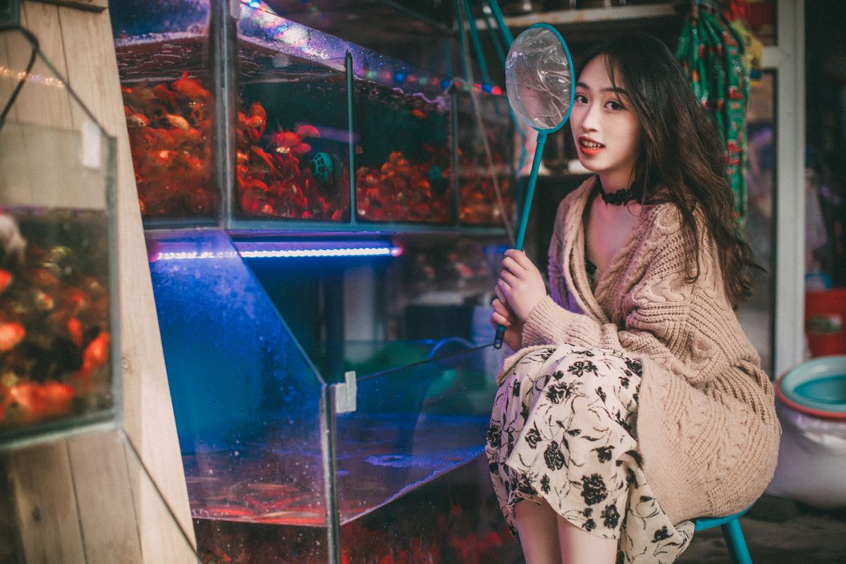 A young woman holding a net beside the fish tanks in a pet shop