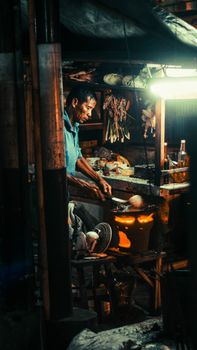 Asian street vendor cooking food in dimly lit night market stall, creating an authentic local dining experience.