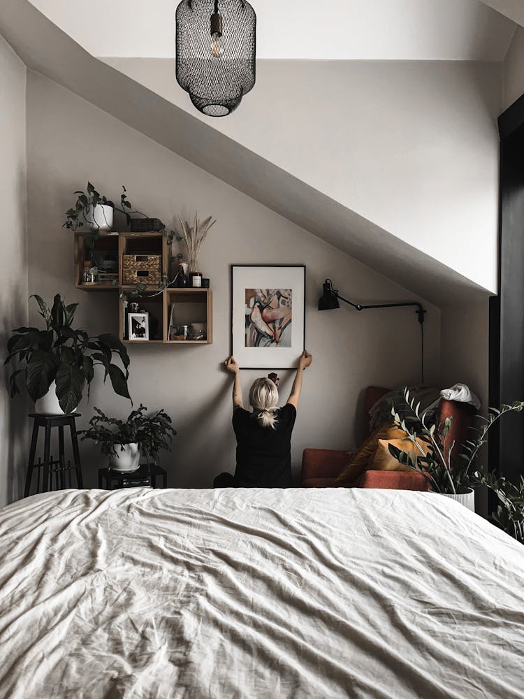 Woman Hanging A Painting In Her Bedroom